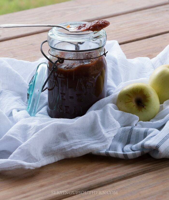 Jar of apple butter sitting on white dish towel with some a couple of apples.