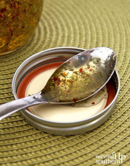 A spoon coated with Garlic Pepper Jelly resting in a mason jar lid.