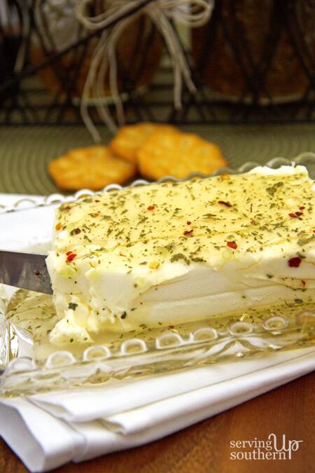 Garlic Pepper Jelly spread over a block of cream cheese with crackers on the side.