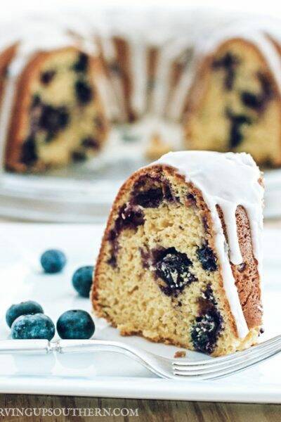 Piece of blueberry bundt cake on a white plate sitting on a wooden board