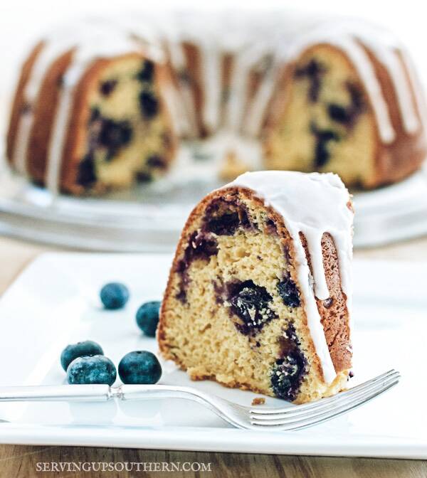 Piece of blueberry bundt cake on a white plate sitting on a wooden board