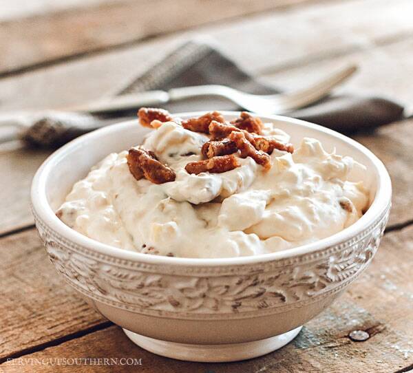 Pineapple pretzel salad in a pretty white bowl with a gray cloth napkin and silver fork on a wooden pallet board.