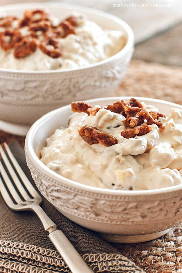 Two pretty white bowls filled with pineapple pretzel salad with a cloth gray napkin and a silver fork.