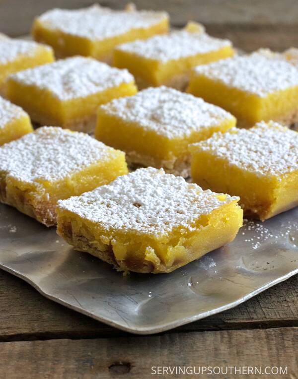 Whole lemon bars dusted with powdered sugar served on a silver platter