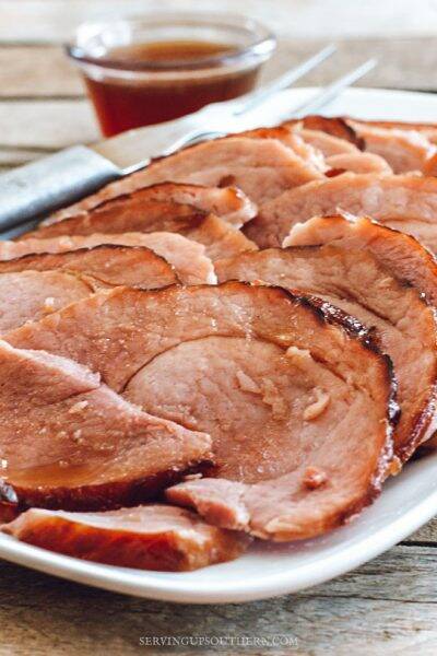 Baked ham on a white serving tray drizzled with pineapple glaze.