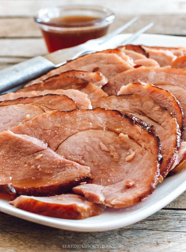 Oven-baked ham on a white serving tray drizzled with pineapple glaze.