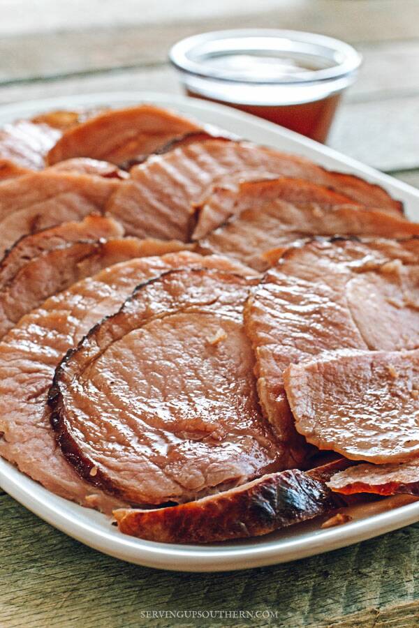 Oven-baked ham on a white serving tray drizzled with pineapple glaze.