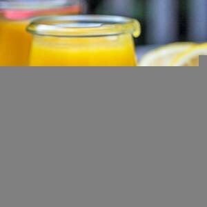 Open jar of lemon curd and a spoonful of curd sitting on a wood board with lemons in the background.