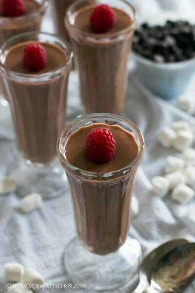 Four elegant glass pudding cups filled with chocolate mousse and topped with a raspberry.