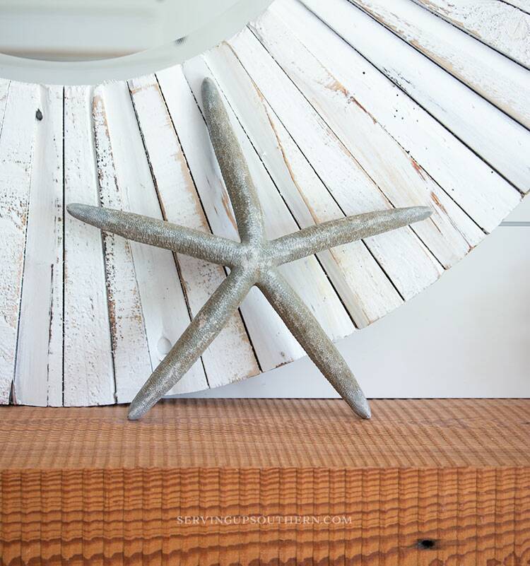 A starfish leaning against a round mirror on a fireplace mantle.