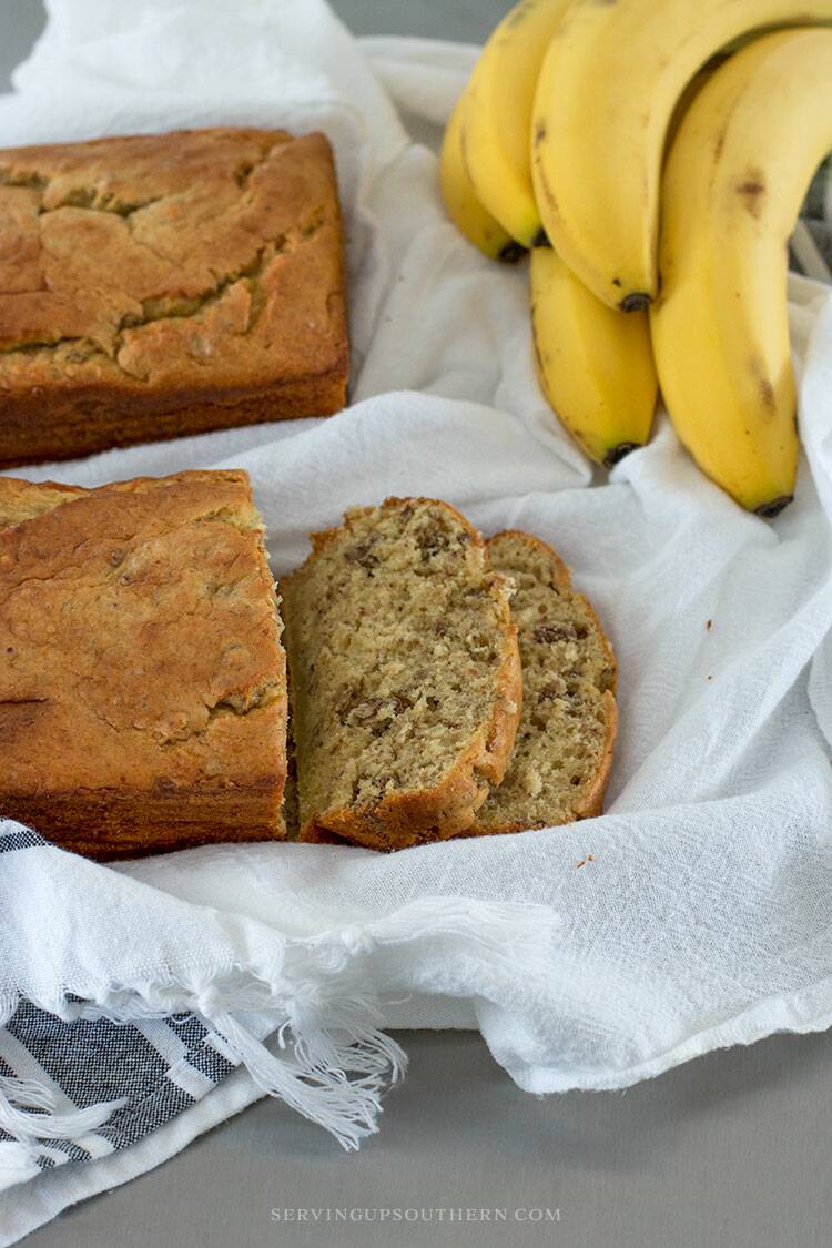 Two loaves of banana nut bread on flour sack towels sitting on a stainless steel island top.