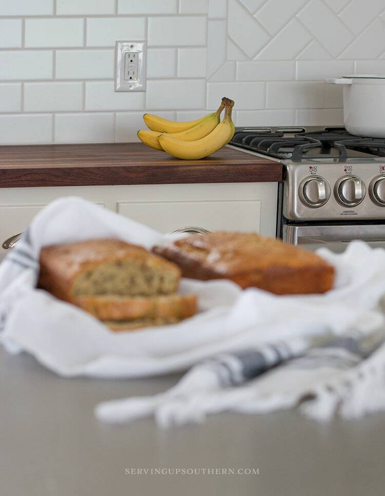 Two loaves of banana nut bread on flour sack towels sitting on a stainless steel island top.