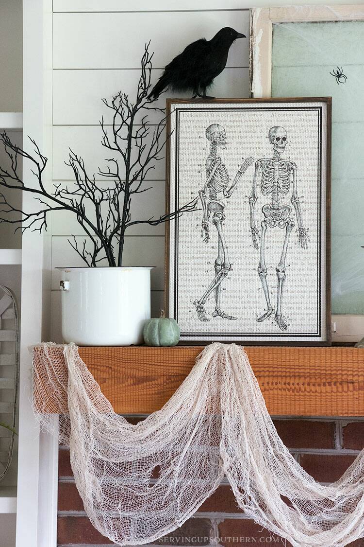 A mantel decorated with black crows, a human skeleton picture, a spider web with spiders, and pumpkins.