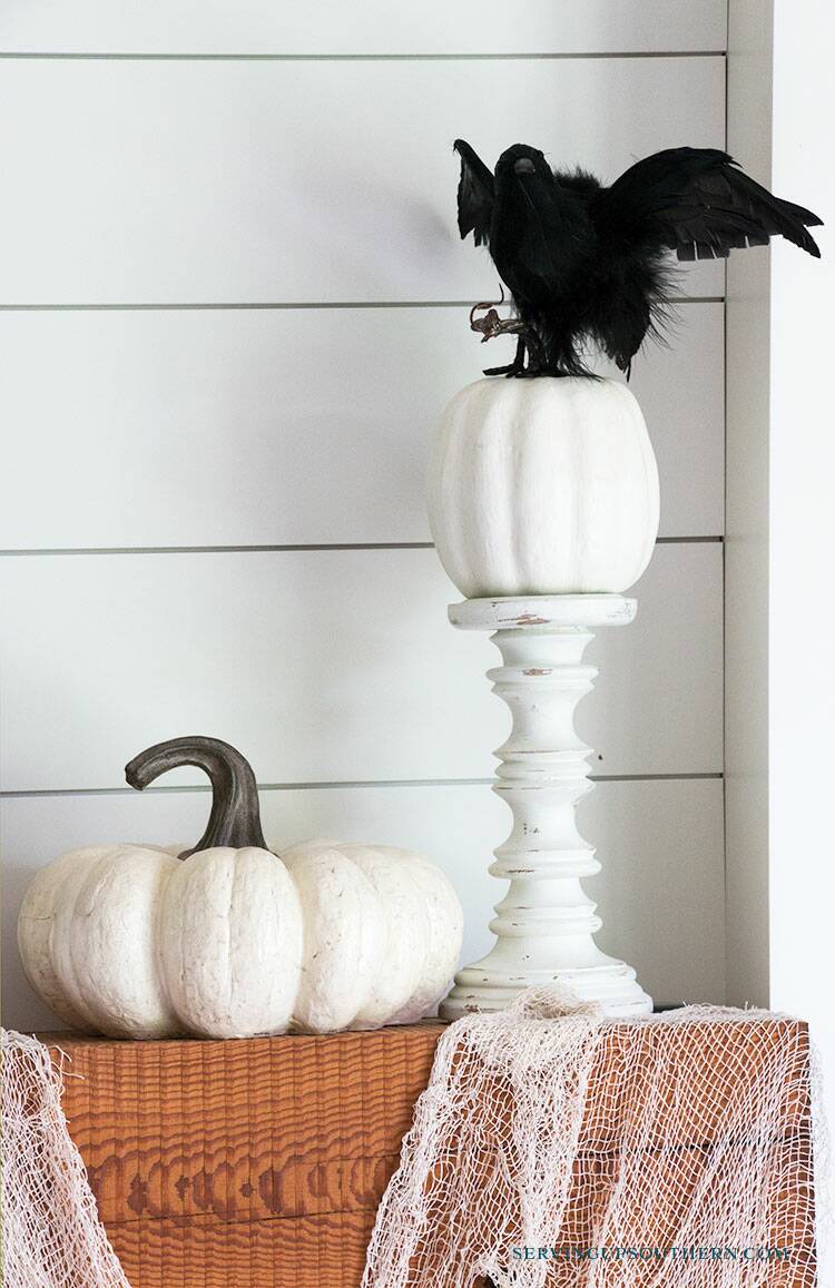A mantel decorated with black crows, a human skeleton picture, a spider web with spiders, and pumpkins.