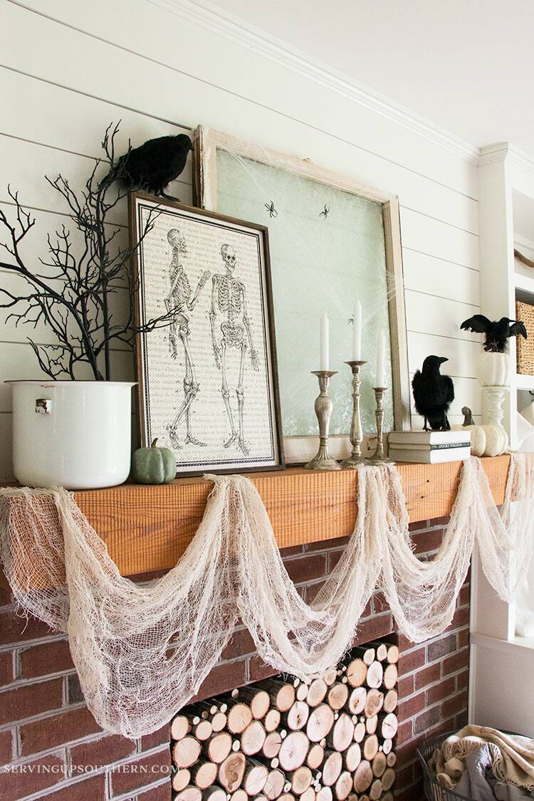 A mantel decorated with black crows, a human skeleton picture, a spider web with spiders, and pumpkins.