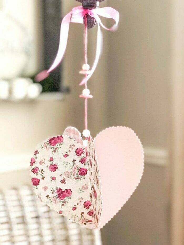 A pretty paper heart hanging from a string with lined with a couple of beads.