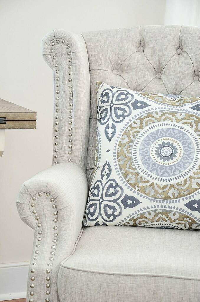 Picture of a cream colored upholstered chair with a white, blue, and green pillow.