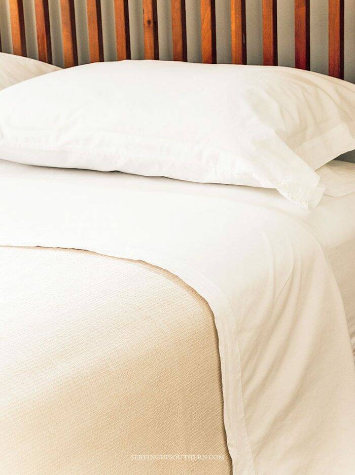 Bed made with crisp white ironed sheets and a cream colored blanket.