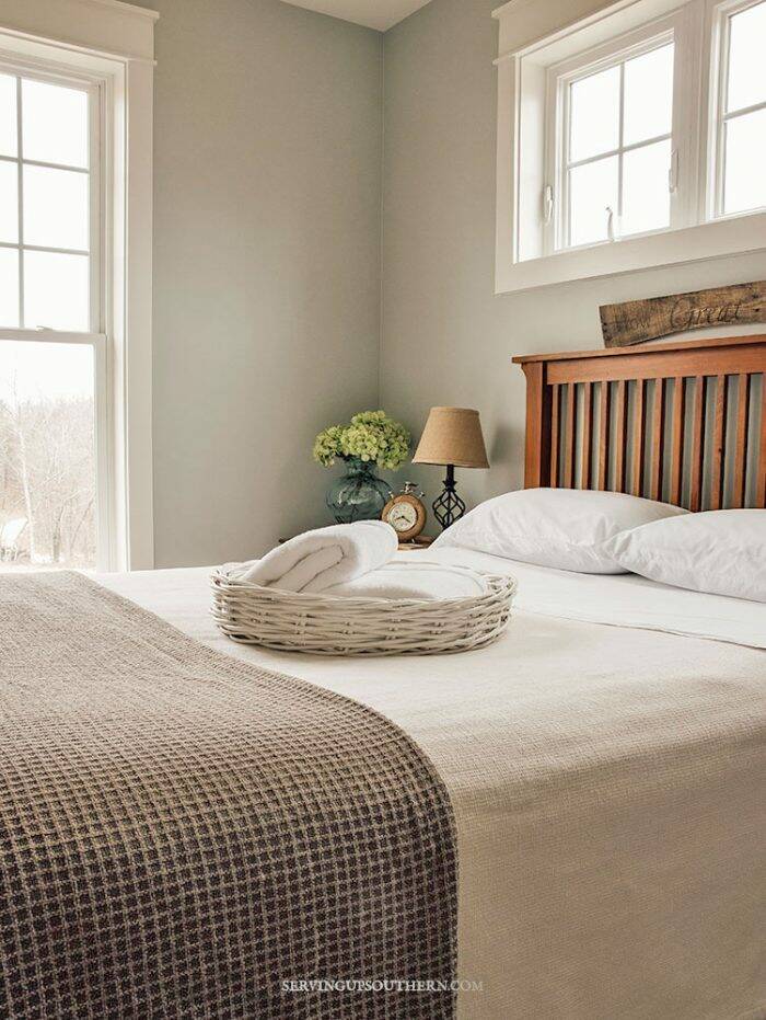 White wicker basket with white fluffy towels sitting on a guest bed with crisp white sheets.