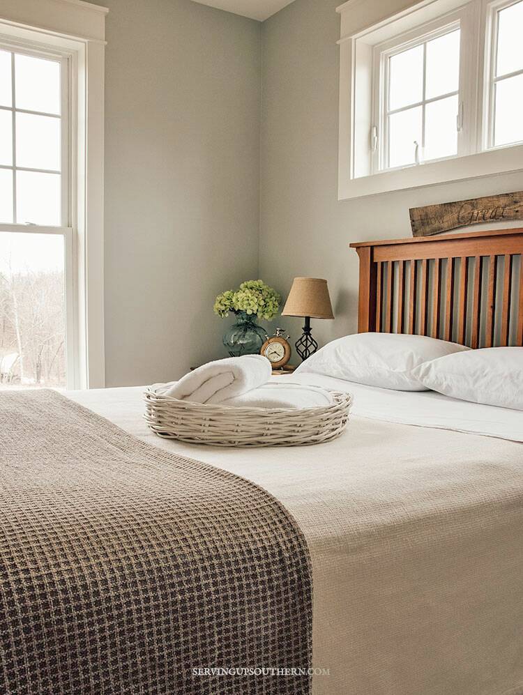 White wicker basket with white fluffy towels sitting on a guest bed with crisp white sheets.
