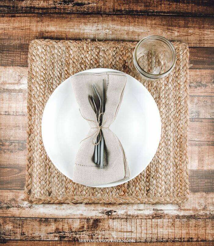 A rustic place setting with a white plate and a mason jar on a wooden board.