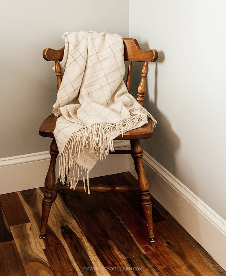 Wooden chair sitting in a guest room with a soft cream throw thrown over the back.