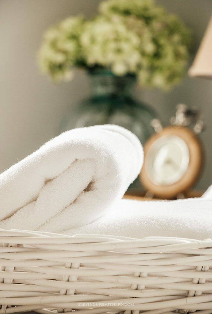 Fluffy white towels in a white wicker basket sitting on a bed.