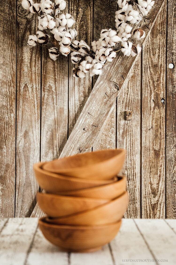 A stack of wooden salad bowls on a white wood board with a weathered door in the background.