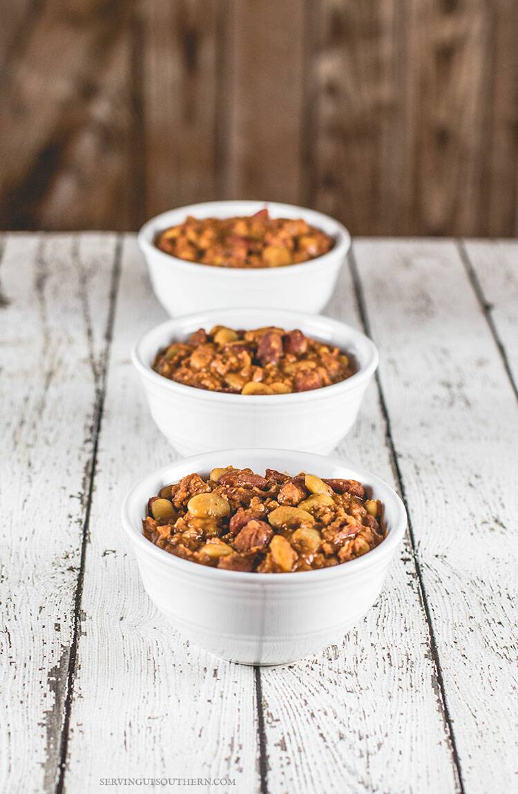 Three bowls of calico beans in white bowls sitting on a white weathered wooden board.