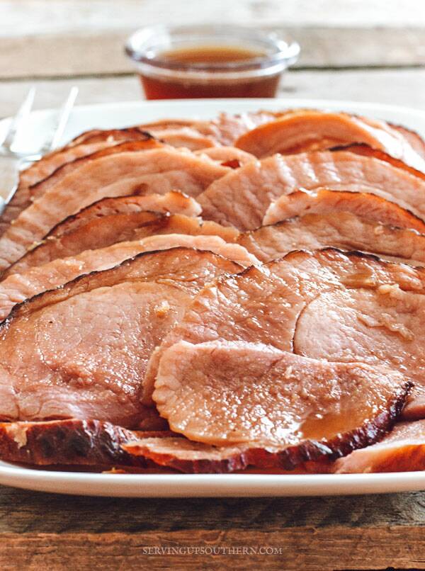 Oven-baked ham on a white serving tray drizzled with pineapple glaze.