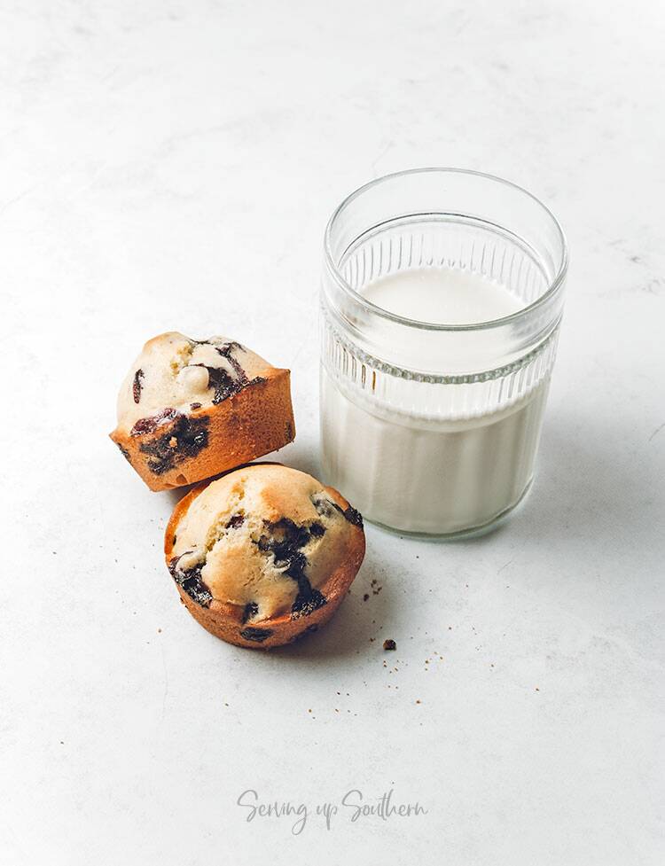 Two blueberry muffins and a glass of milk on a marble surface. 