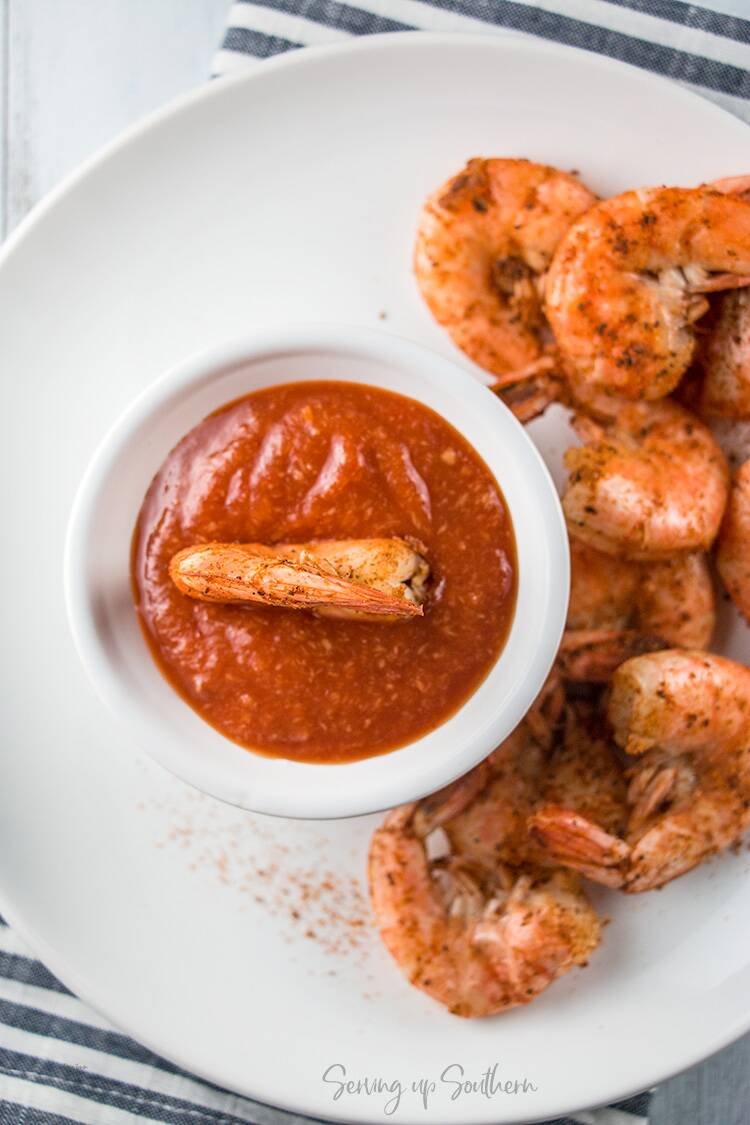 A bowl of cocktail sauce on plate with cooked shrimp