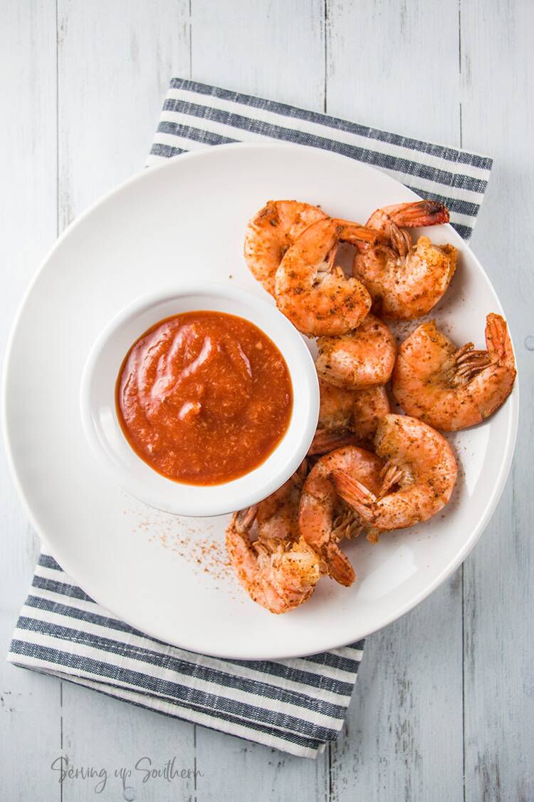 A bowl of cocktail sauce on plate with cooked shrimp