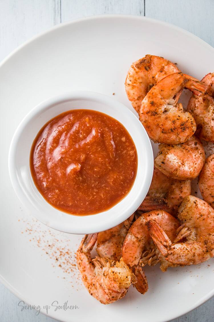 A bowl of cocktail sauce on plate with cooked shrimp