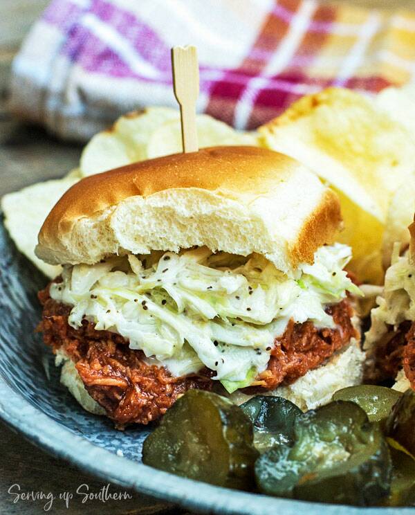 Slow Cooker BBQ Chicken Sliders on a pie tin with chips and pickles.