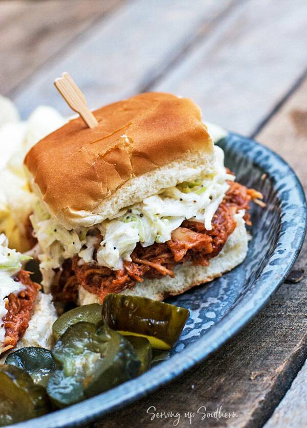 Slow Cooker BBQ Chicken Sliders with coleslaw on a pie tin with pickles and chips.