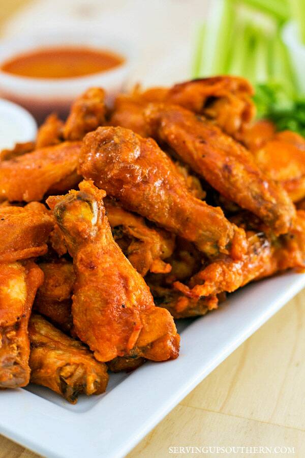 A pile of buffalo wings on a platter with ranch and celery.