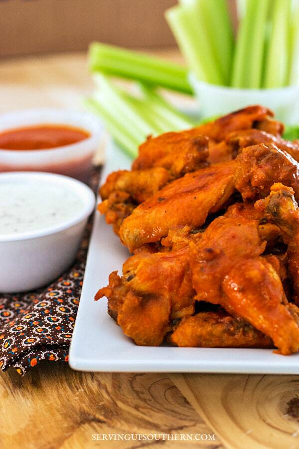 Hot buffalo wings on a platter with celery sticks and ranch dressing.