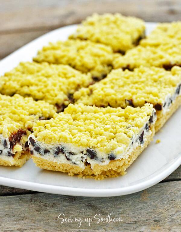 Chocolate Chip Cream Cheese Bars on a white plate sitting on a wooden board