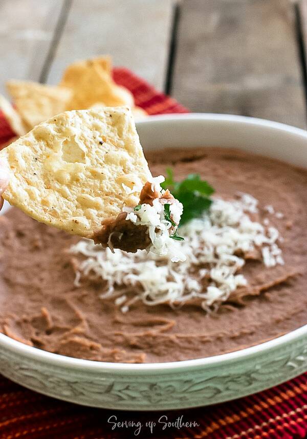 Tortilla chip dipped into a bowl of crockpot refried beans.