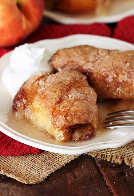 Homemade peach dumplings served on a white plate with cream.