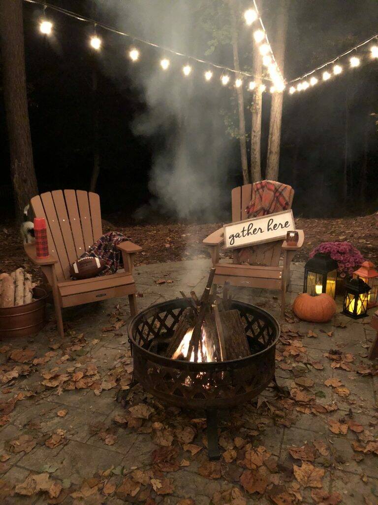 Outdoor fire in firepit with chairs, pumpkins, and cozy blankets.