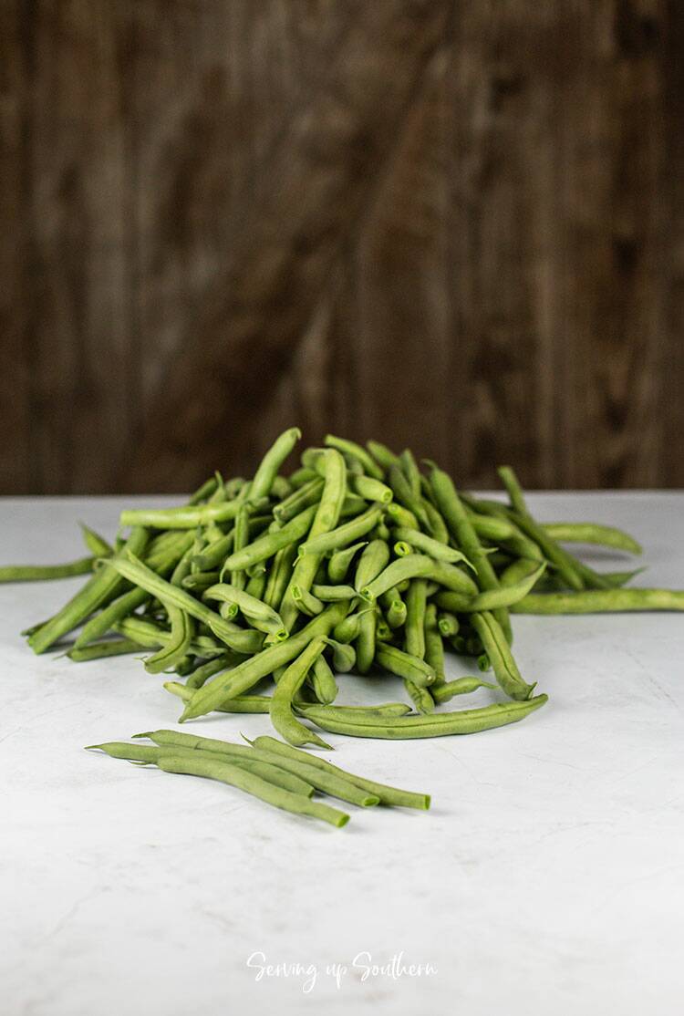 A mess of snapped green beans on a marble surface with a wood background.