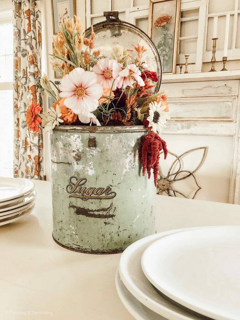 A vintage sugar tin with a beautiful fall arrangement displayed as a centerpiece on table.