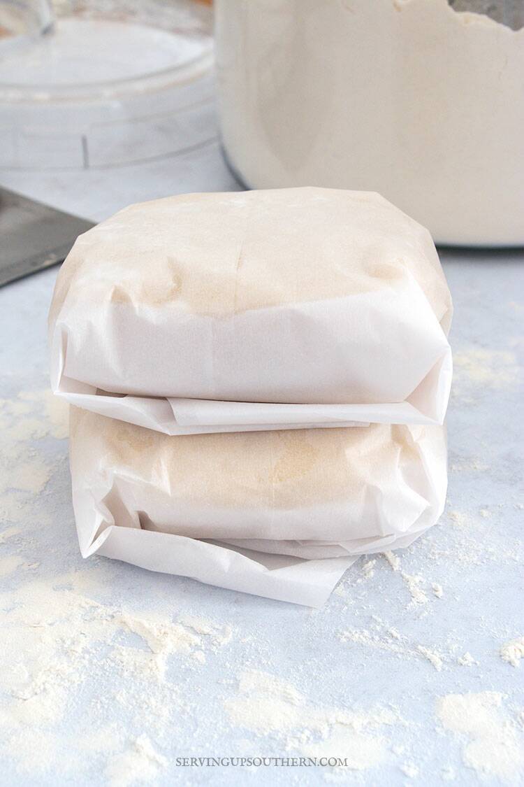 Two disks of homemade pie crust dough wrapped in parchment paper before putting in fridge