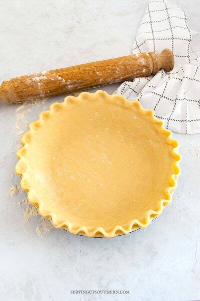 Homemade pie crust pastry in pie plate on marble surface with a rolling pin and tea towel