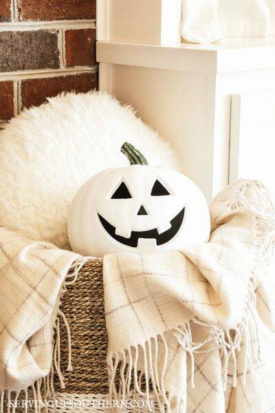 Painted jack o' lantern nestled in a basket with a pillow and throw.