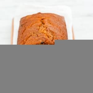 A loaf of sliced pumpkin bread on a wooden cutting board with a gray and rust colored dish towel.