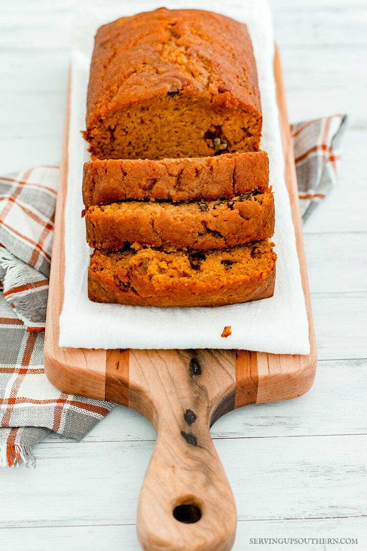 A loaf of pumpkin bread on a wooden cutting board with a gray and rust colored dish towel