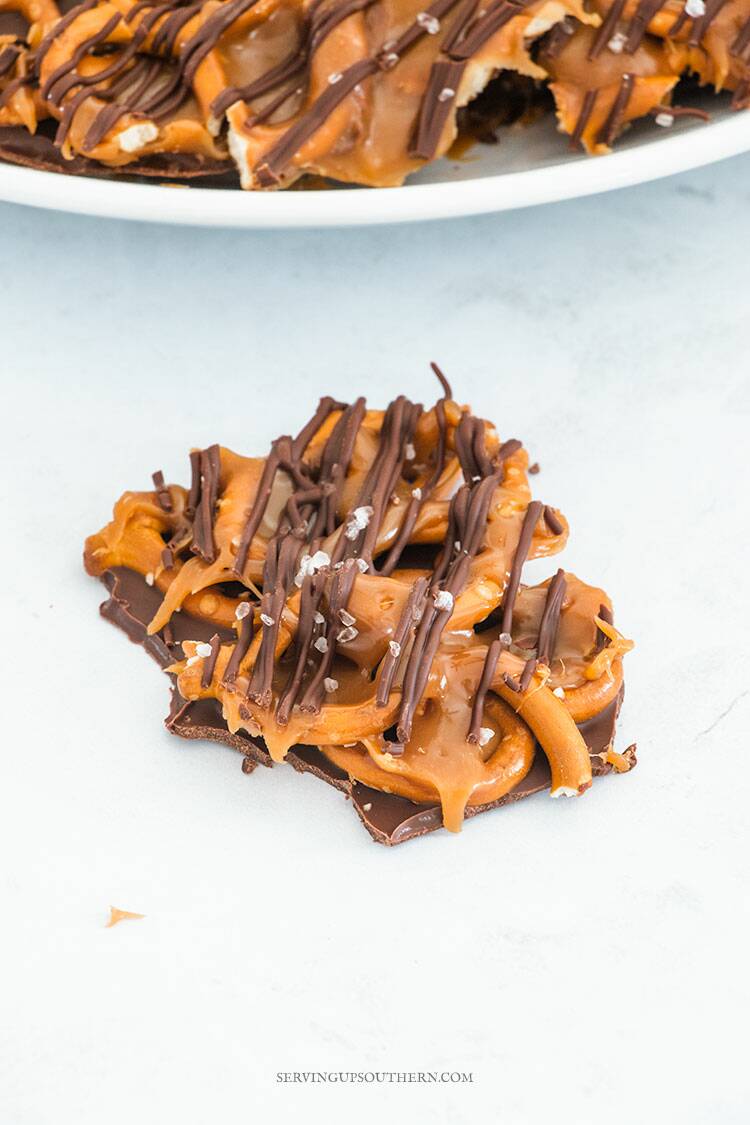 A piece of salted caramel chocolate pretzel on a marble surface with a plateful in the background.